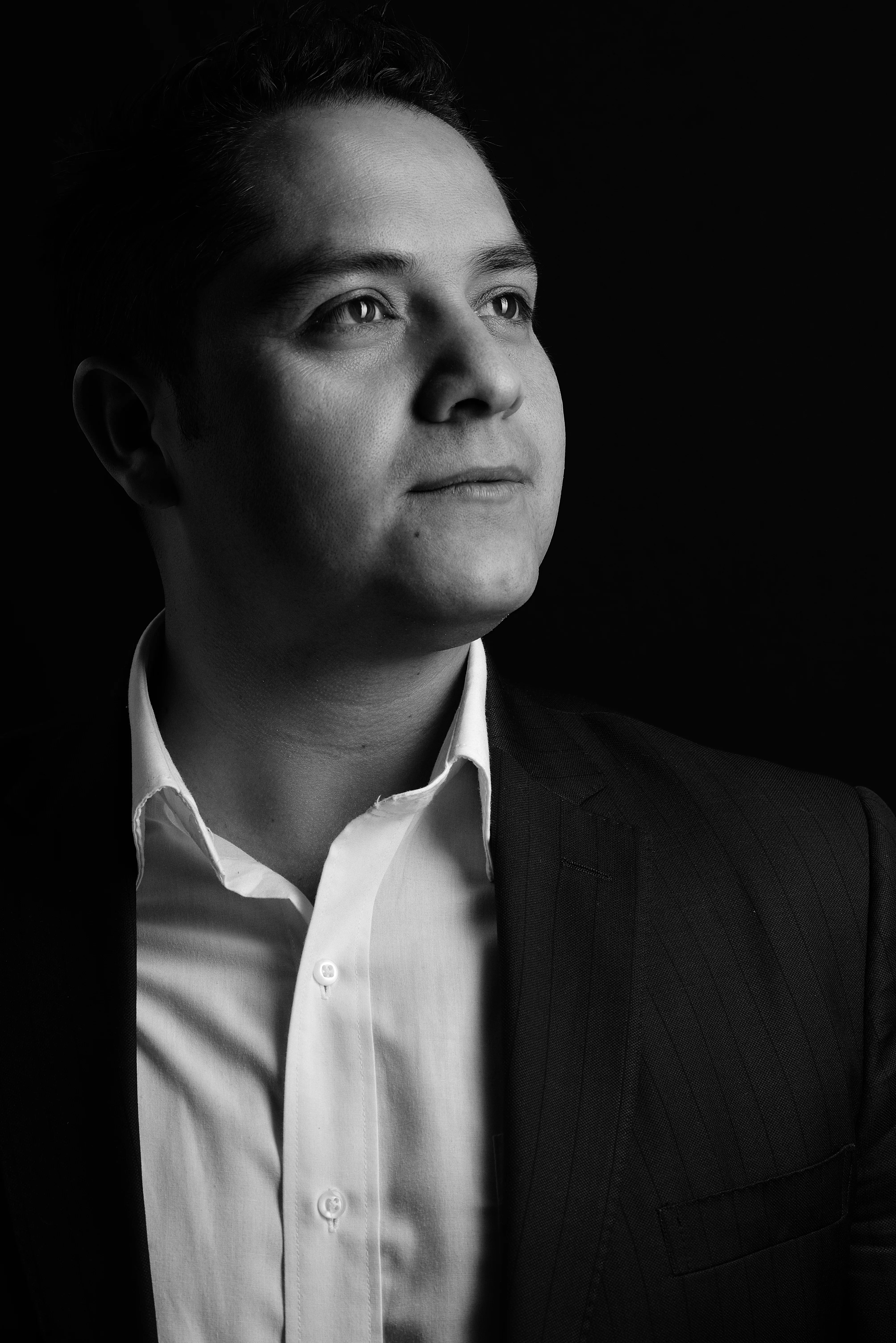 Retrato en blanco y negro de un hombre de saco oscuro y camisa blanca, con luz lateral sobre fondo negro