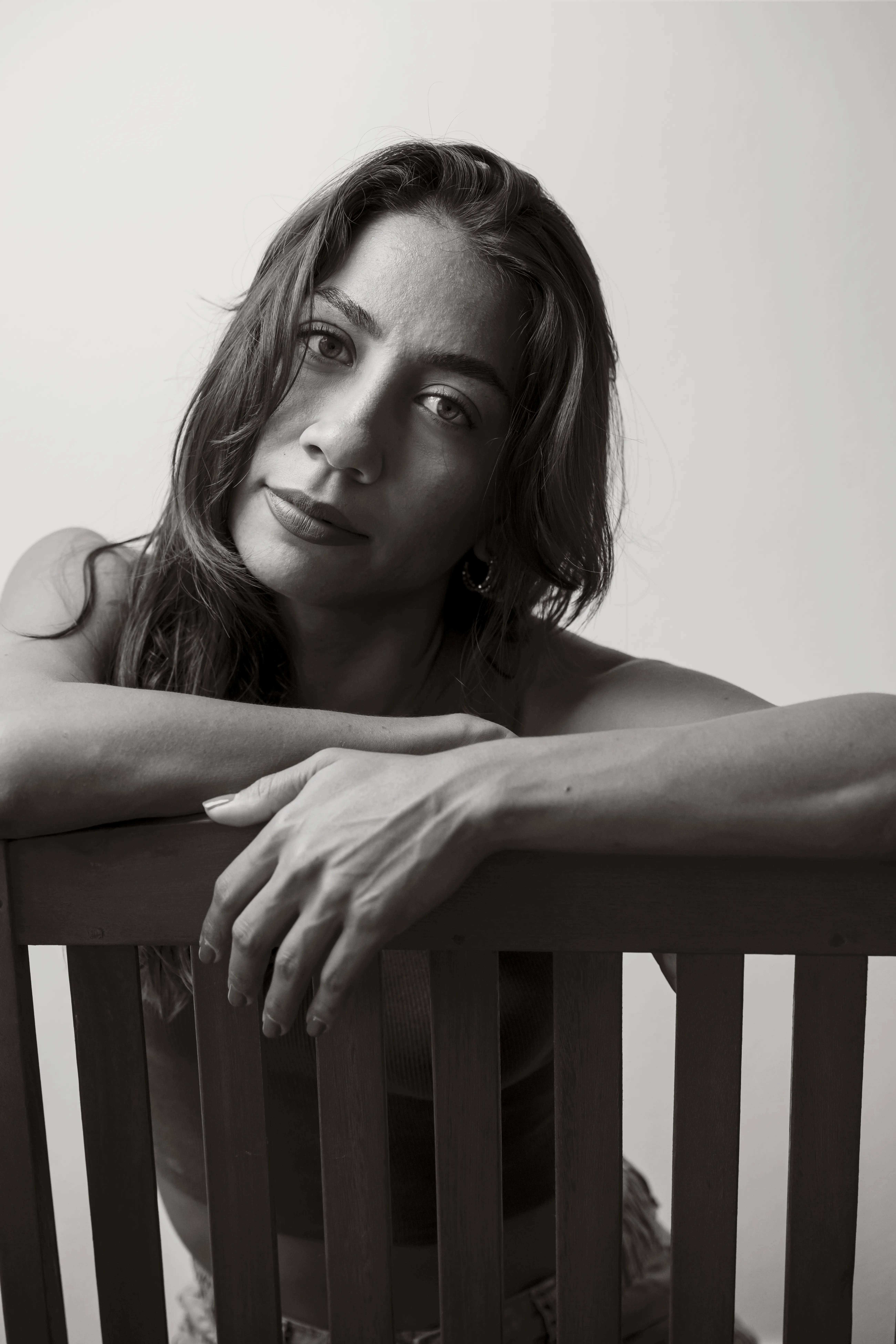 Retrato en blanco y negro de una mujer recargada sobre el respaldo de una silla, con luz suave de estudio