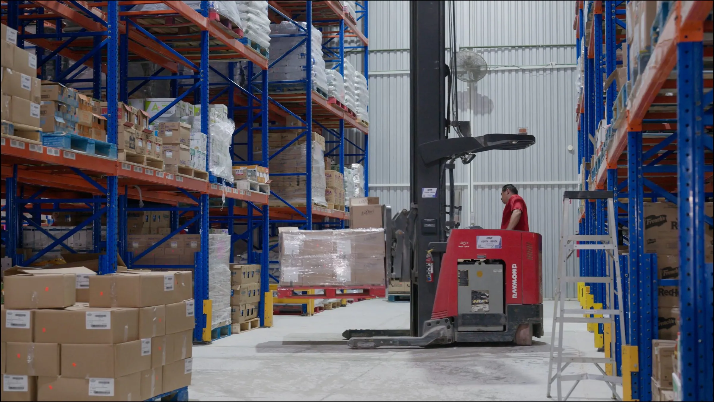 Montacargas elevando tarima entre racks de bodega fría, interior de planta operando