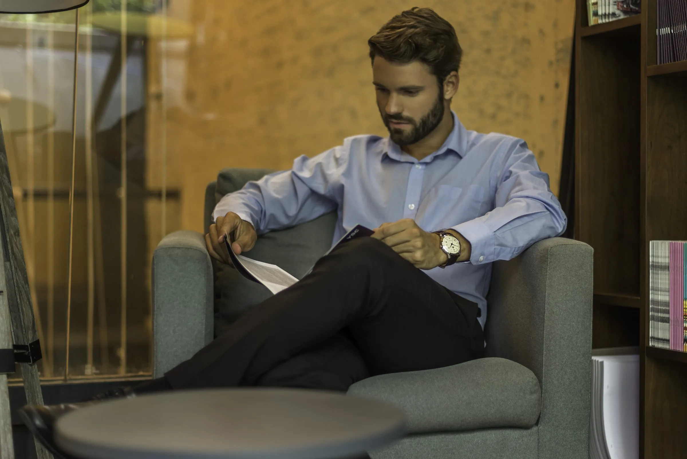Hombre leyendo en sillón de oficina con reloj visible, producto en escena lifestyle con ambientación de contexto de uso