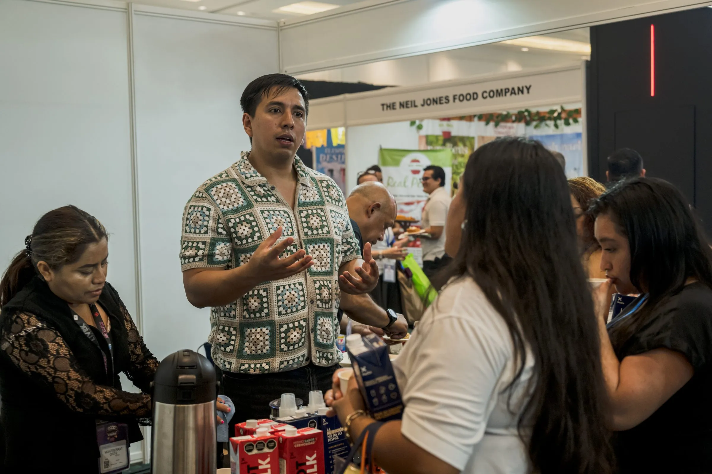 Representante de marca conversando con asistentes frente a su stand, presencia de patrocinador en contexto del evento