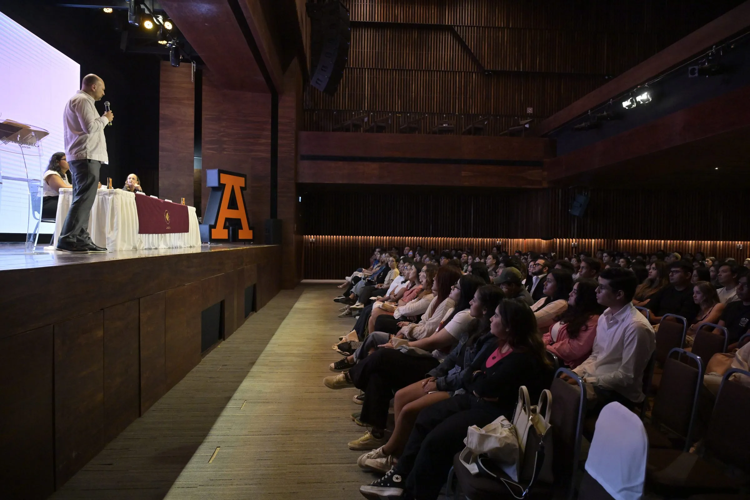 Ponente en escenario durante su presentación en el congreso, audiencia sentada visible