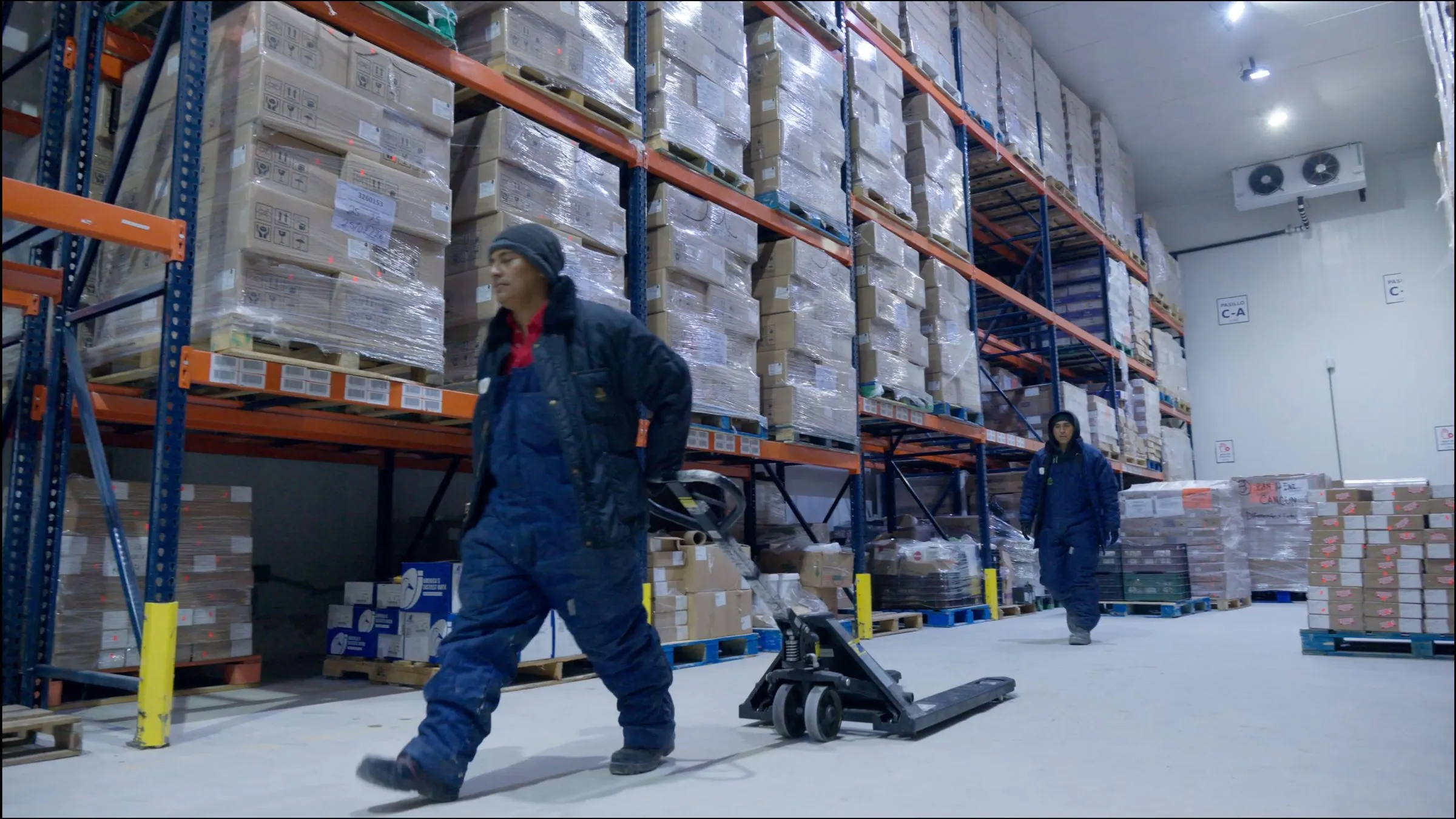 Personal con equipo térmico moviendo carga entre racks de bodega fría, proceso con orden visible