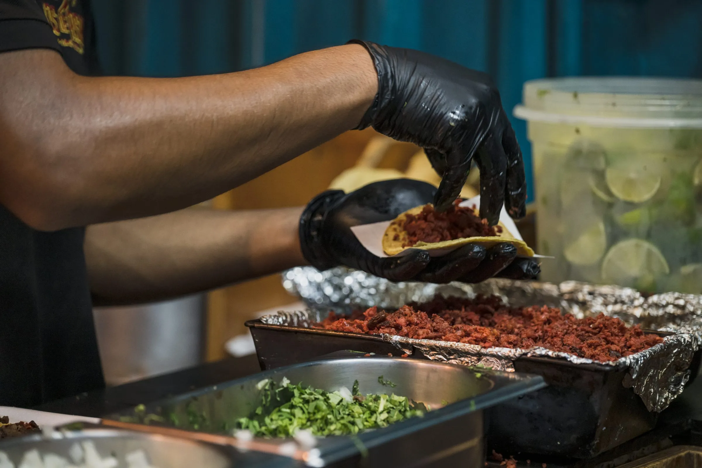 Mano tomando un taco directo de la charola con salsas y limones al lado, el momento real de servicio, no posado para cámara