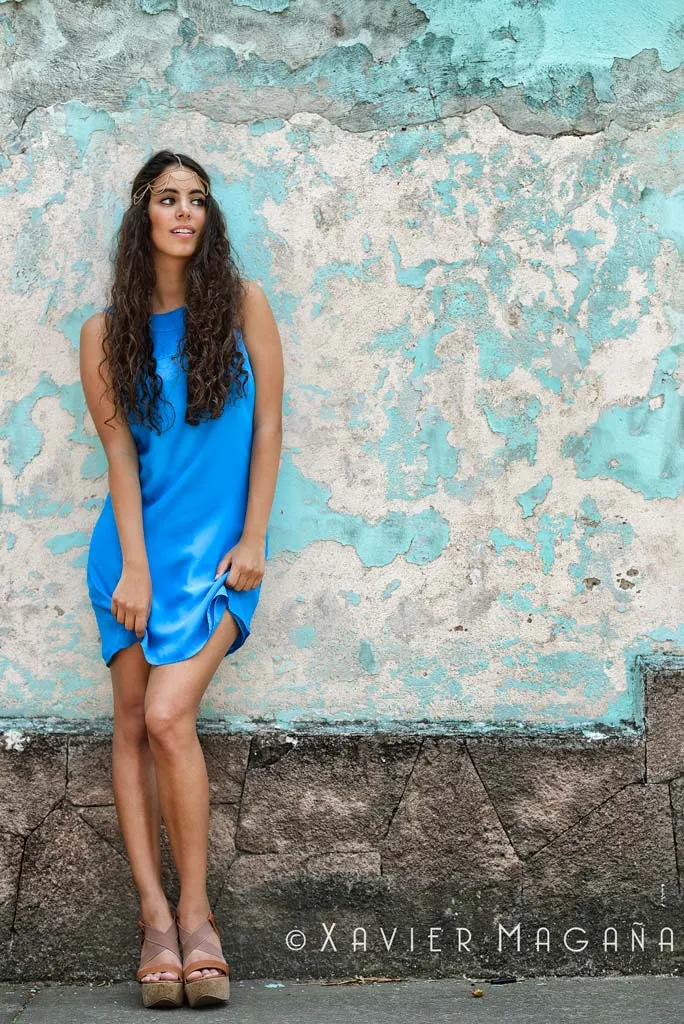 Mujer con vestido azul posando frente a un muro turquesa desgastado