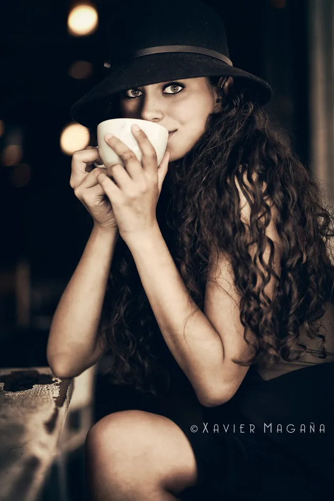 Mujer con sombrero sosteniendo una taza entre las manos, luz cálida de interior