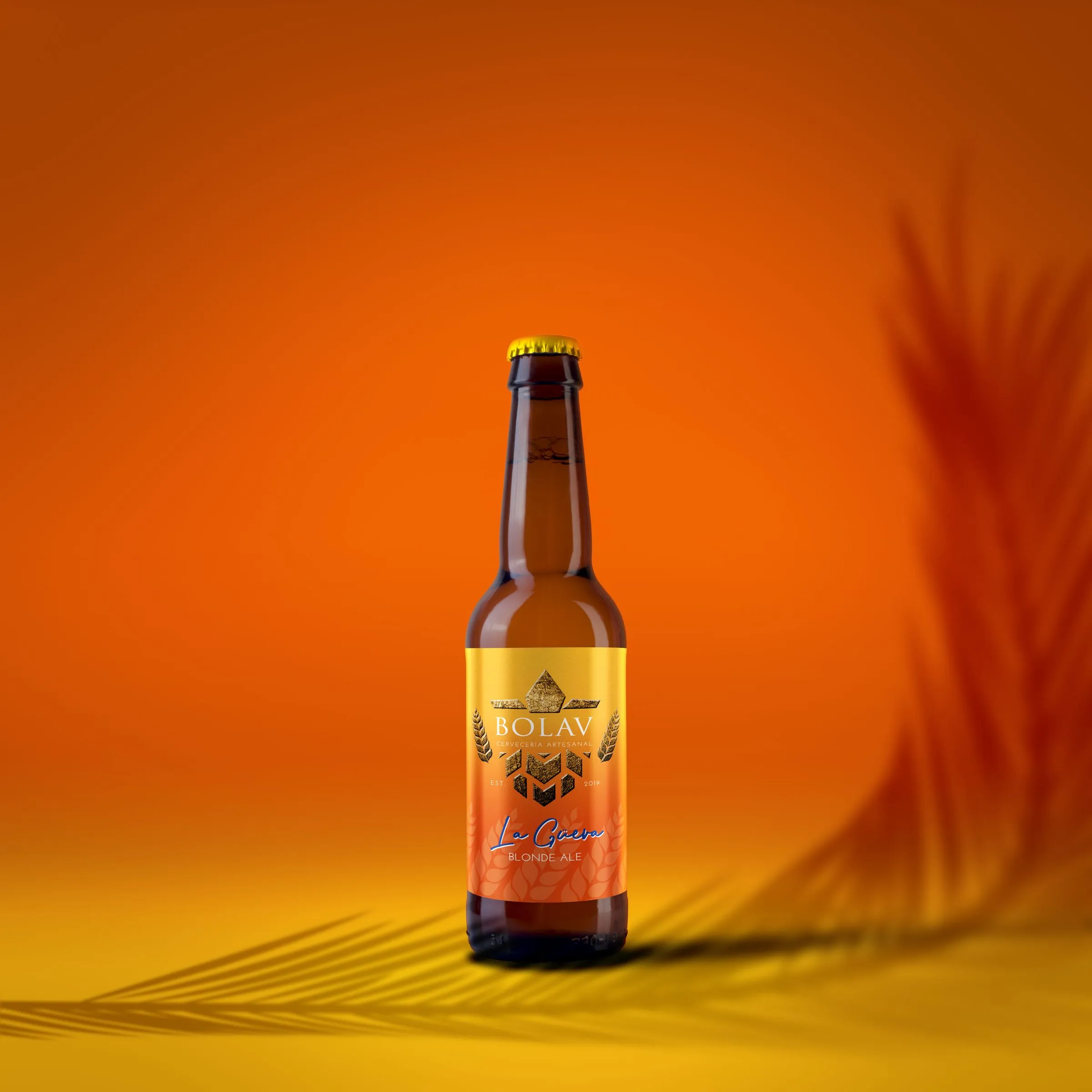 Bottle of La Güera Blonde Ale beer with a gold label, photographed against a gradient orange background with blurred wheat stalks
