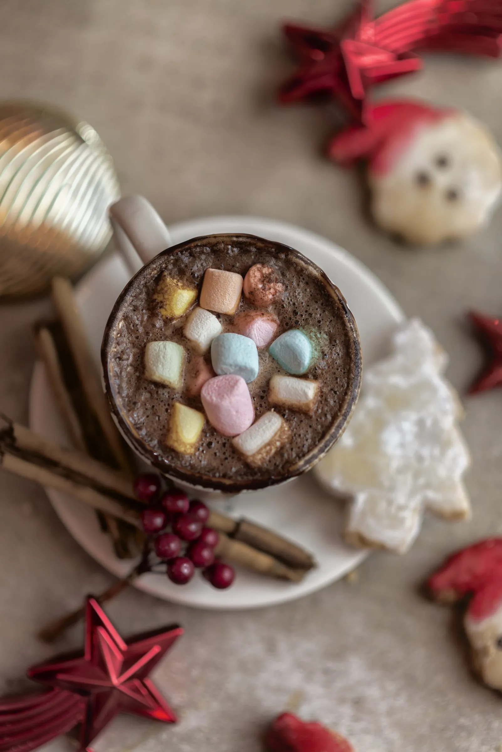 Chocolate caliente con malvaviscos fotografiado desde arriba, rodeado de esferas navideñas, estrellas decorativas y una galleta con forma de Santa Claus.