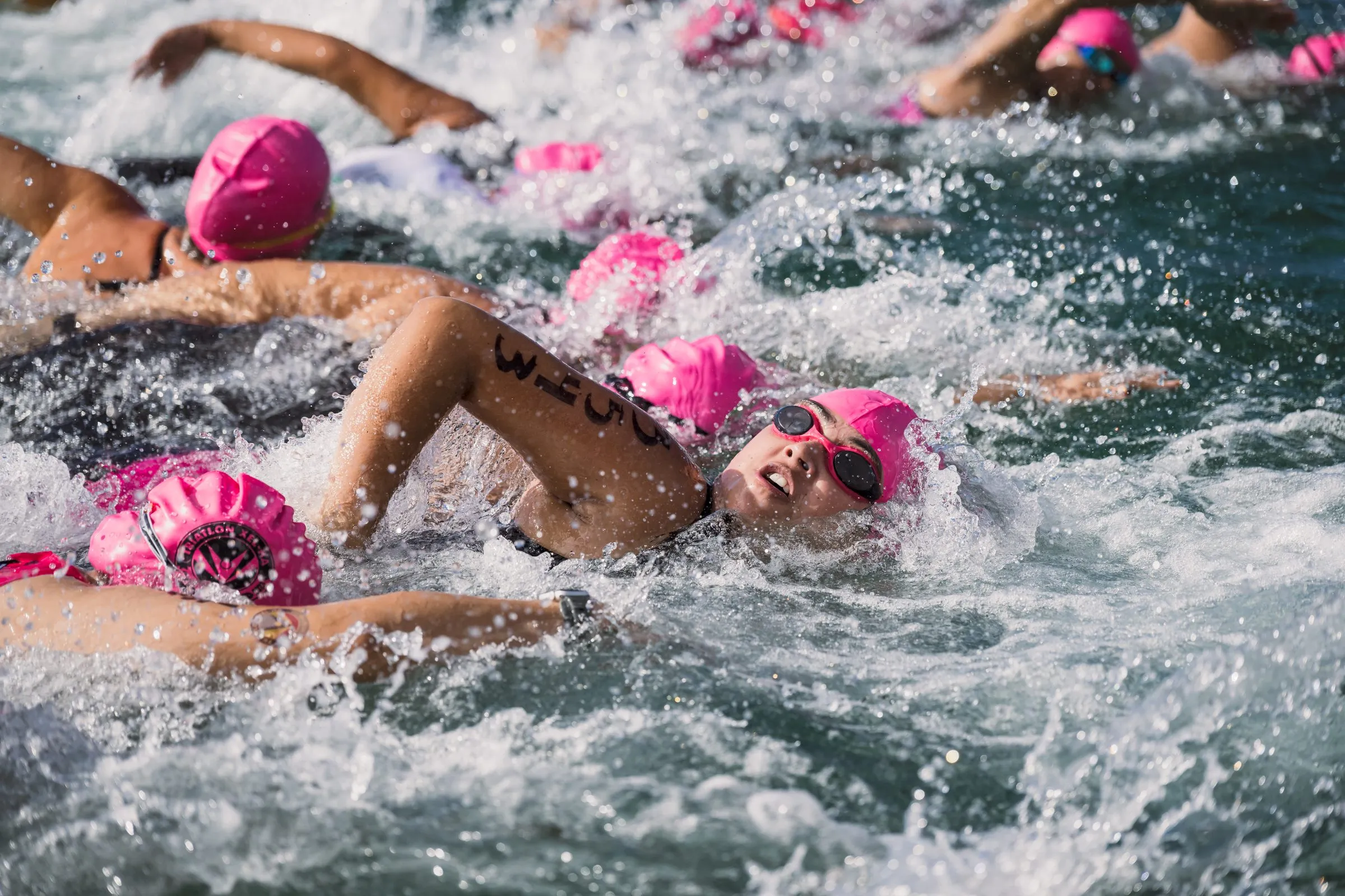 Nadadoras en pleno esfuerzo bajo luz dura y directa durante el tramo de natación del triatlón