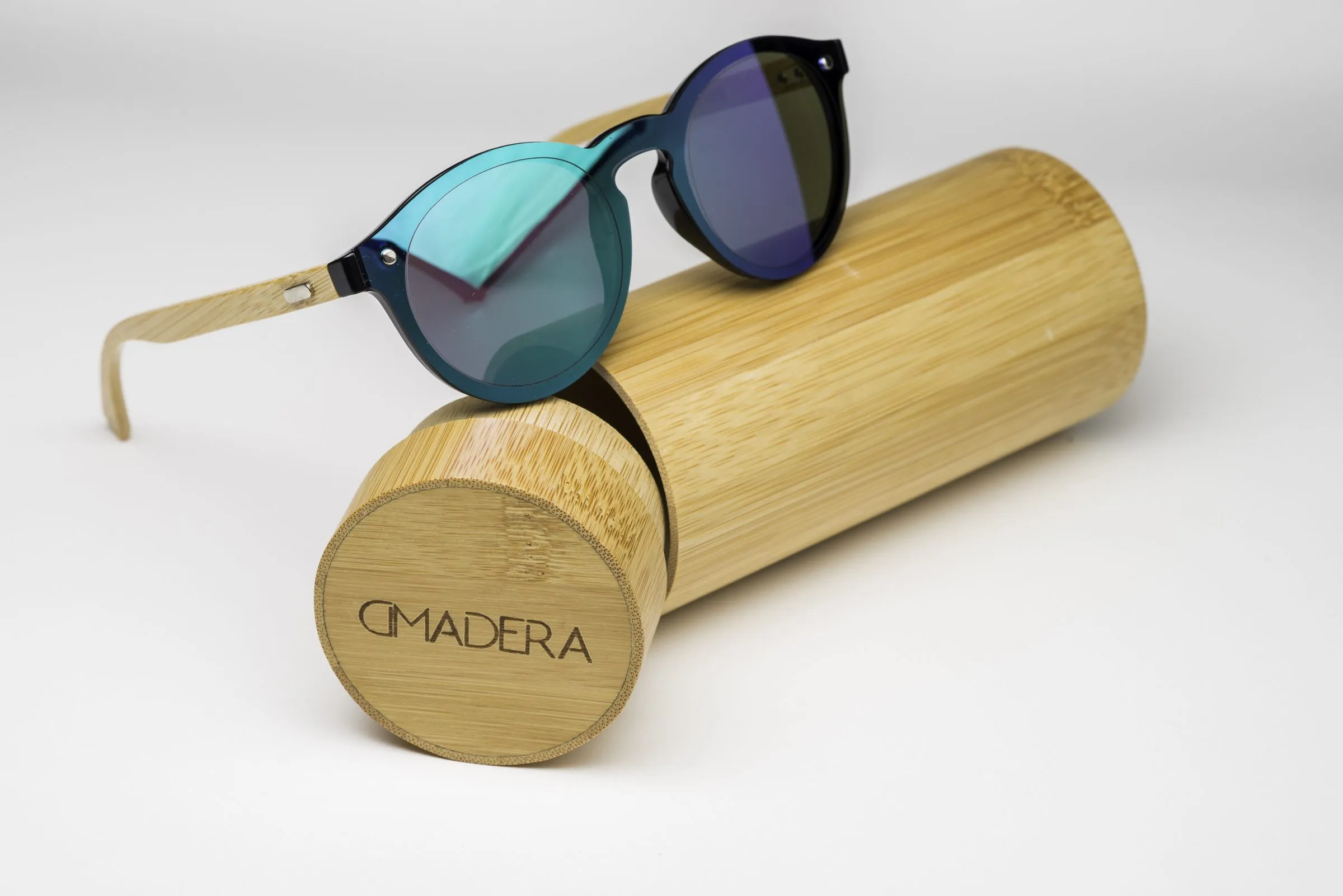 Round sunglasses with a navy-black front and lenses mirrored from teal to purple, wooden temple arms, resting on a cylindrical wooden case.