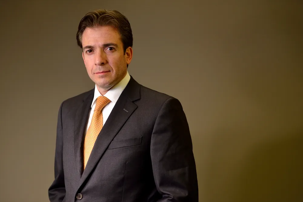 Retrato corporativo de un ejecutivo de traje gris y corbata dorada, de pie sobre fondo verde olivo