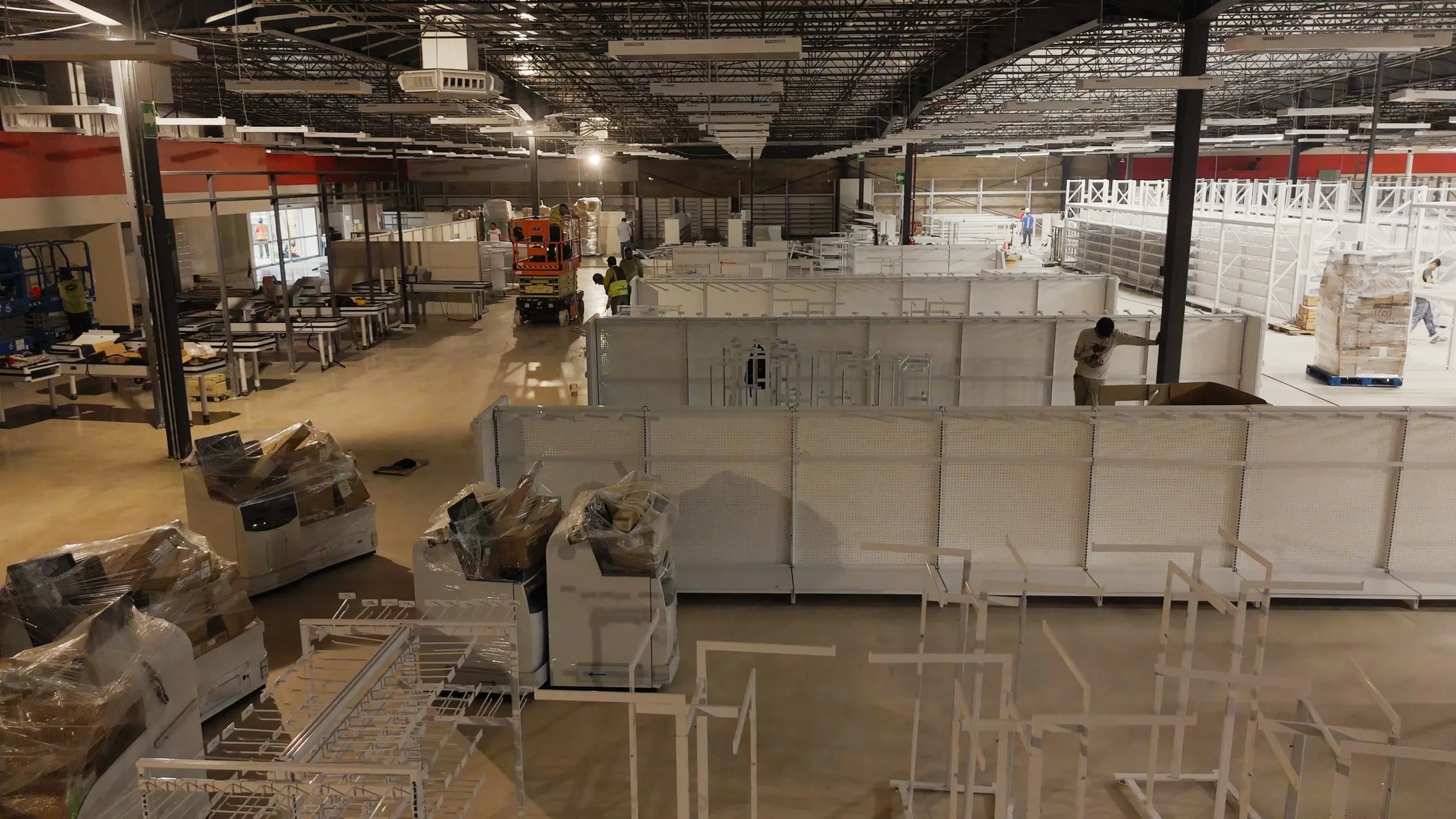 Retail floor mid fit out with modular white shelving units being assembled by workers, a scissor lift visible in the background