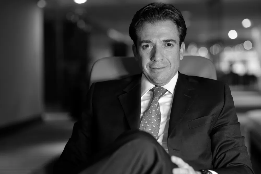 Retrato en blanco y negro de un ejecutivo de traje sentado en una sala de oficina, en actitud relajada
