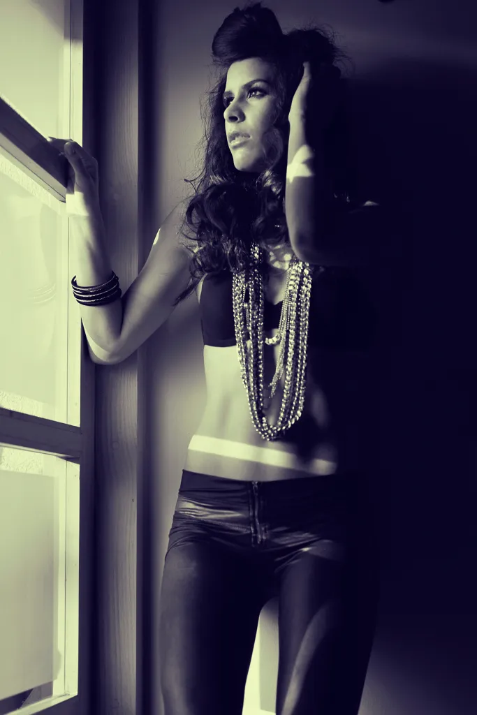 Retrato de moda a contraluz de una mujer junto a un ventanal, con collares de perlas.