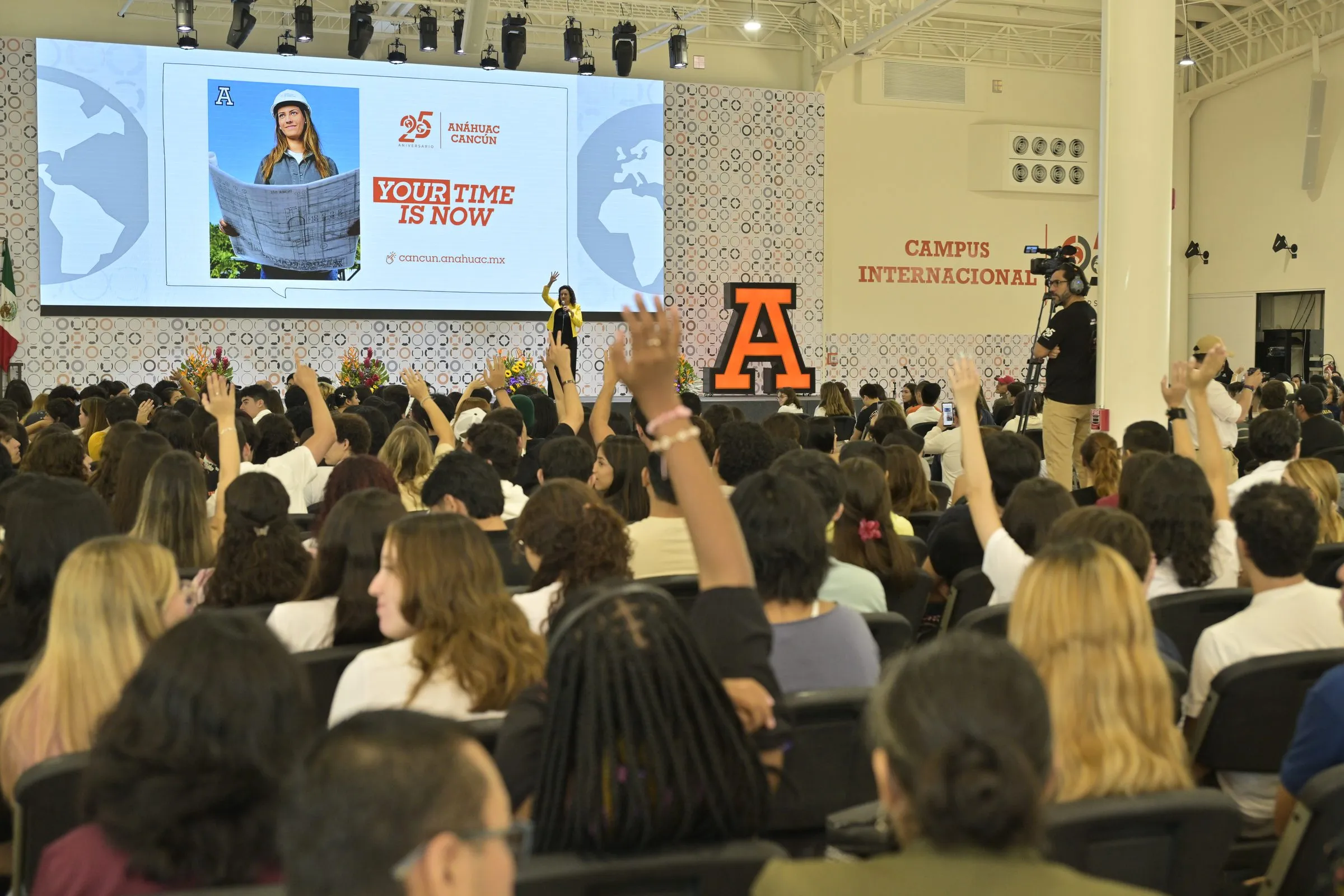 Auditorio lleno de estudiantes con las manos levantadas durante un evento institucional en la Universidad Anáhuac Cancún
