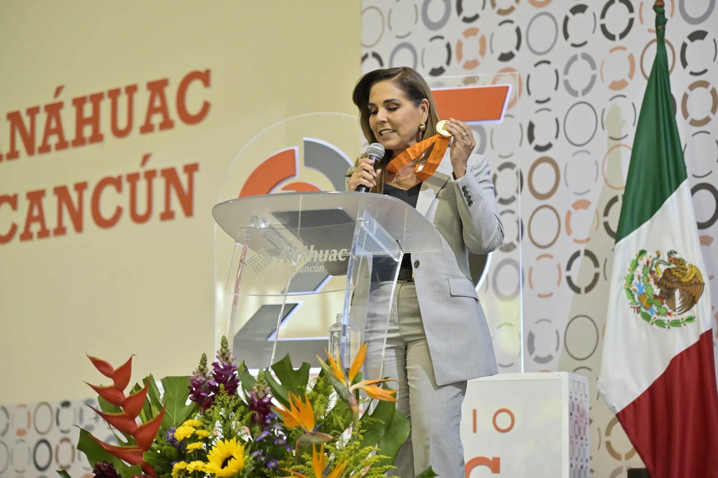 Speaker at a podium with a Mexican flag and university branding, key moment of a conference in Cancun