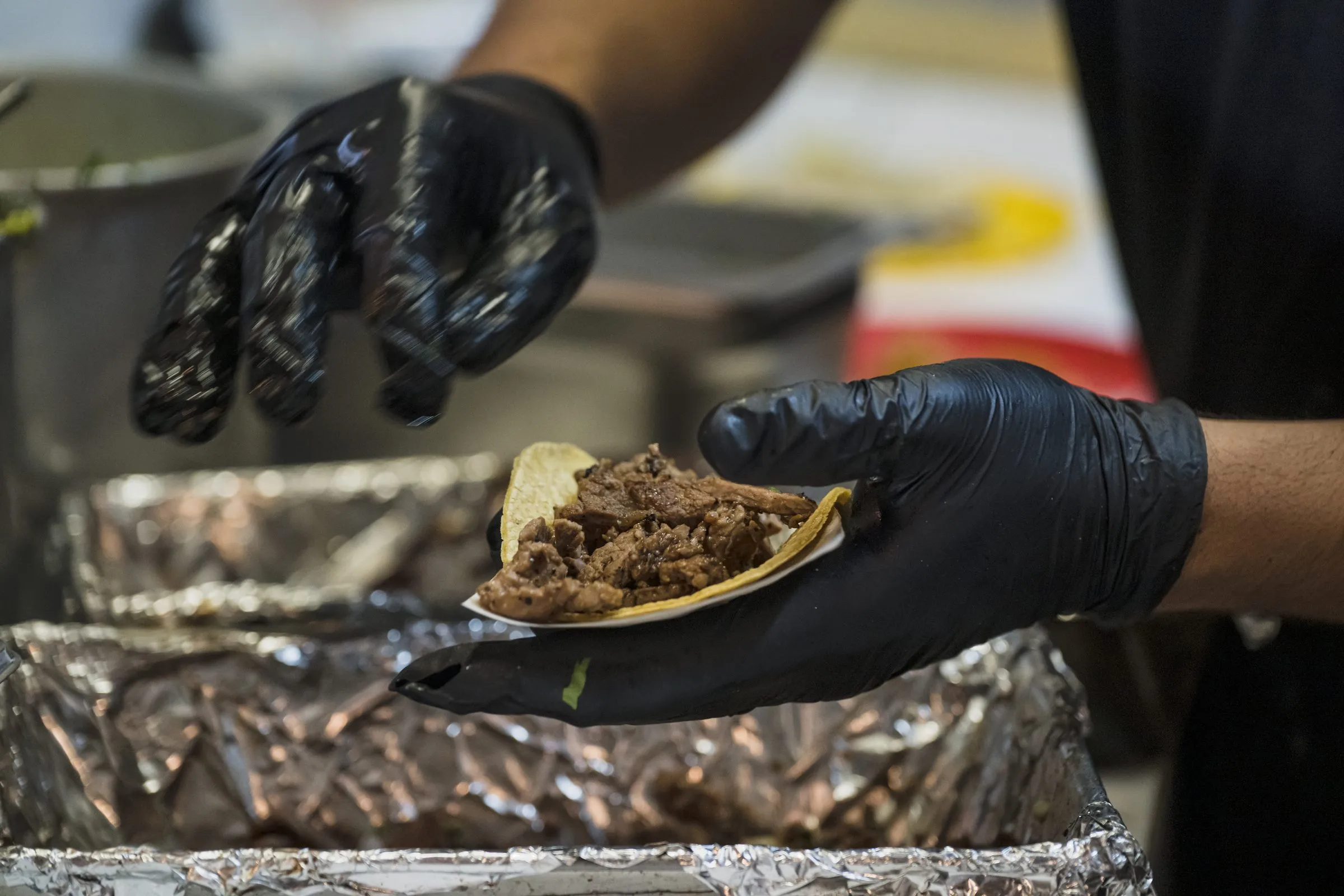 Mano enguantada sosteniendo un taco recién armado en papel aluminio, taquería de brasas real en Cancún